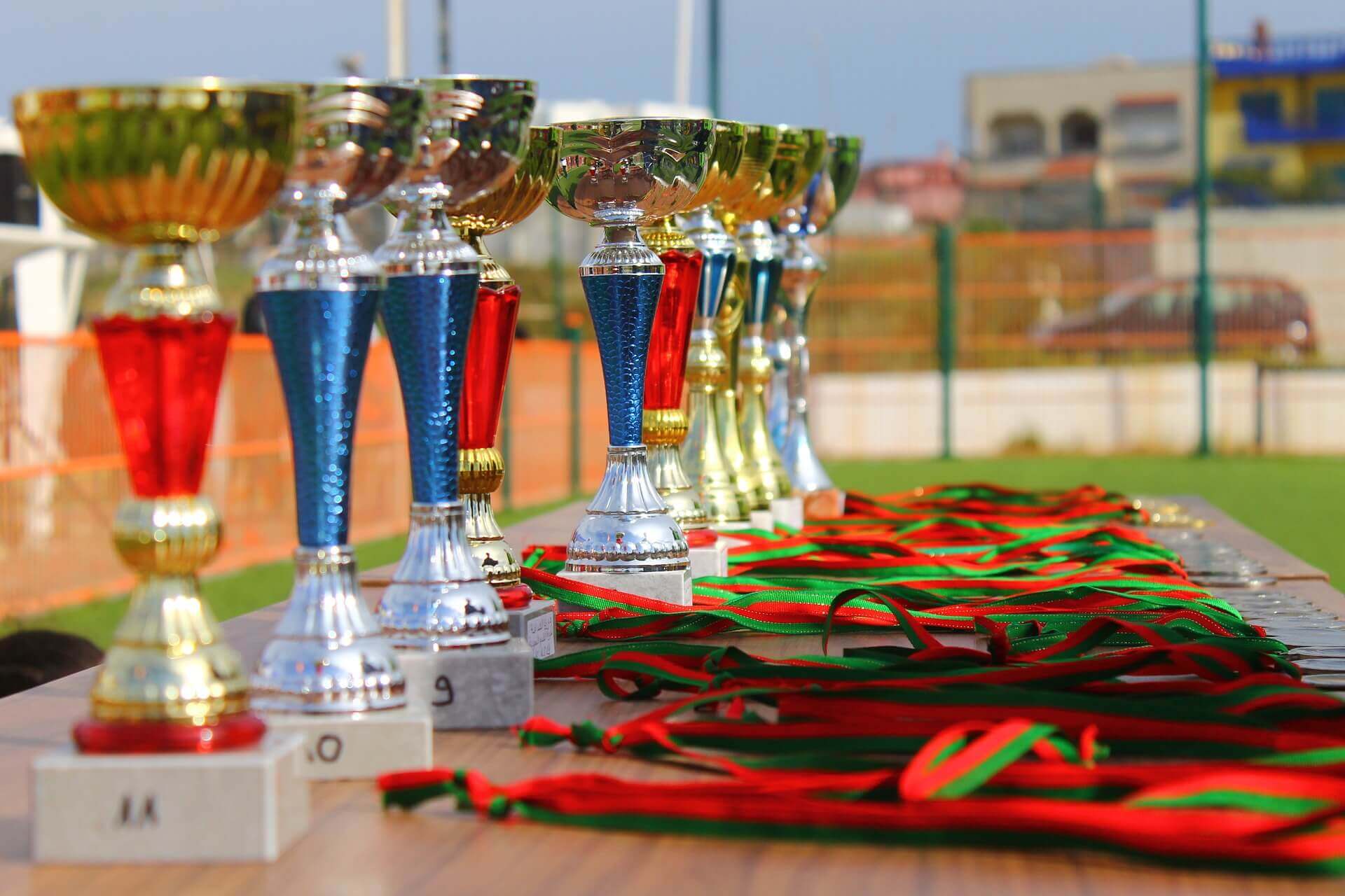 A row of silver and gold trophies on a table with green-and-red ribbons